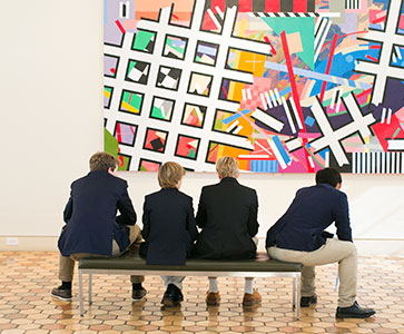 Students sitting on a bench in an art gallery. Links to Gifts by Will